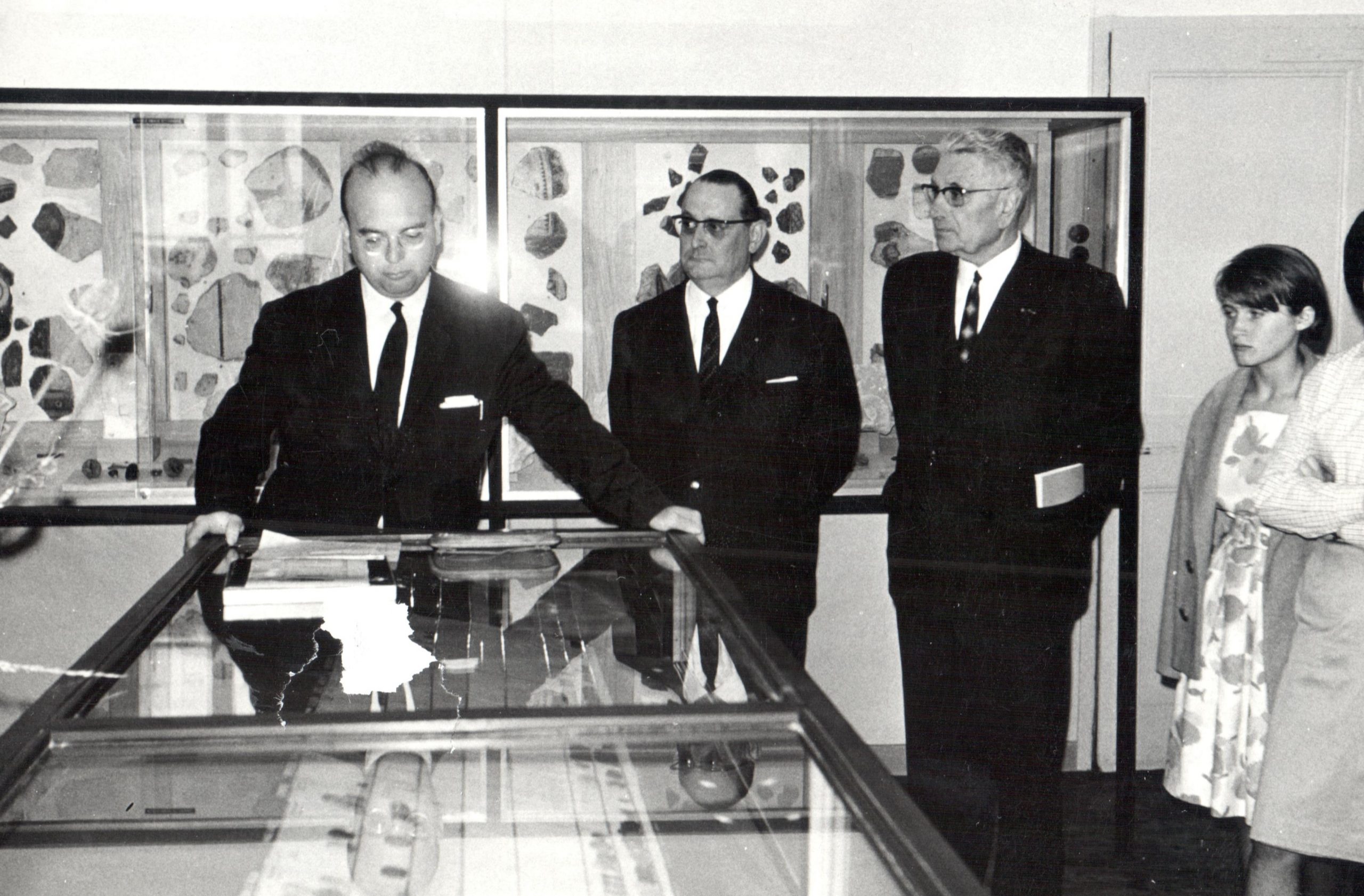 Raymond Chevallier inaugure la nouvelle présentation du musée archéologique d’Izernore le 17 juillet 1966. Au premier et à l'arrière-plan, on voit des vitrines. Au milieu, 3 hommes en costumes et deux femmes sont présents. La photo est en noir et blanc.