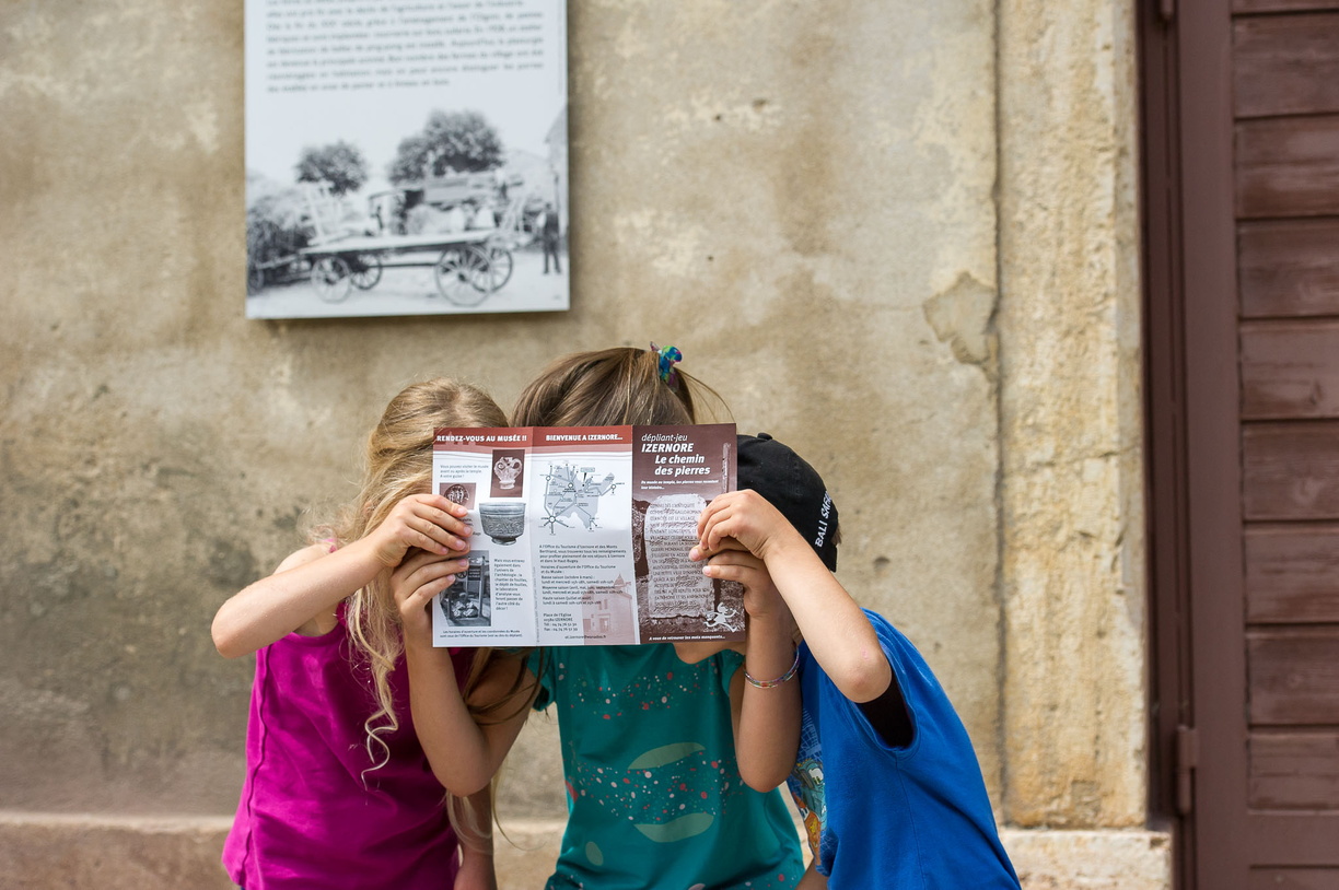 3 enfants en visite au cœur du village. Ils lisent tous ensemble le dépliant du "Chemin des pierres"